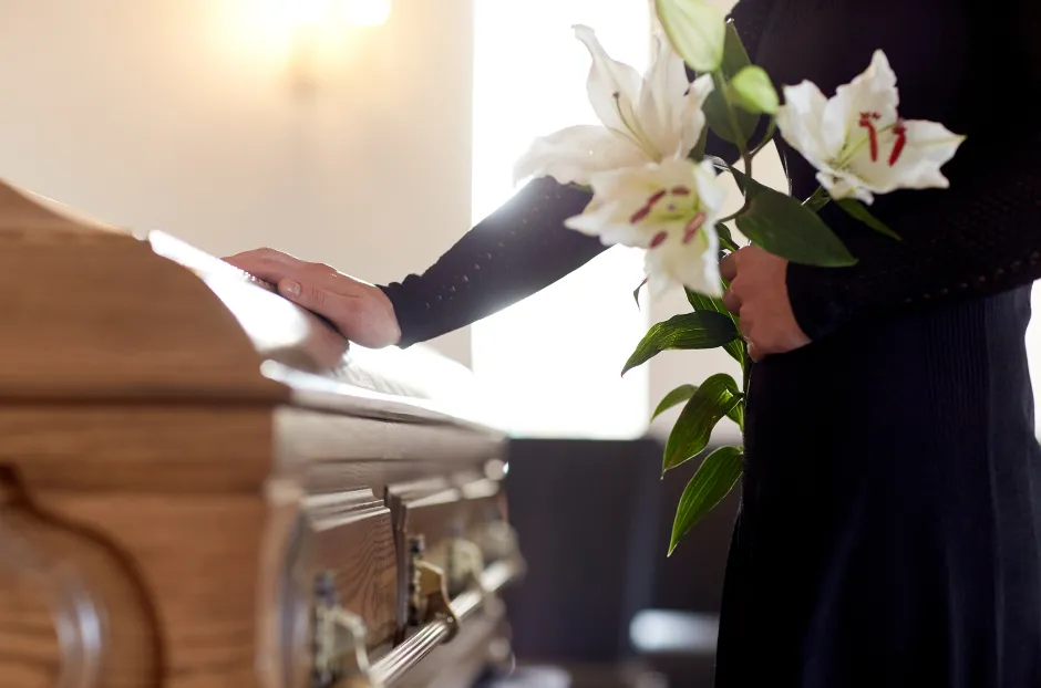 A casket laid out with a lady in black touching it and saying goodbye to their loved on whilst holding roses and playing a piece of modern funeral music to celebrate their life lived