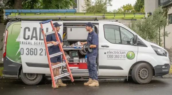 Smiling First Call Electrical electricians holding electrical equipment and ladders with an open branded van