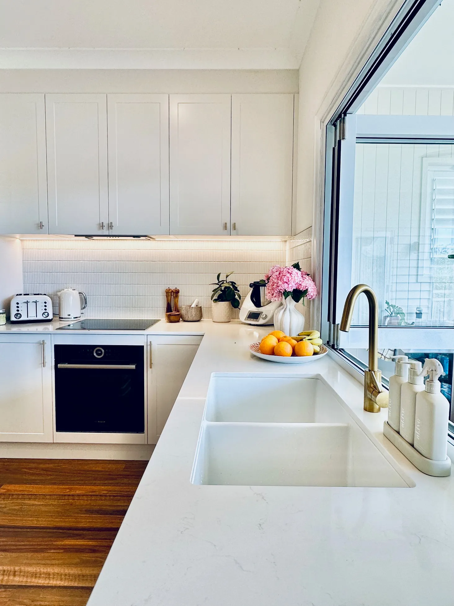 Haddon Kitchens installed  wood matt laminate benchtops with ‘Charmed White’ satin cabinetry tied together with brushed brass handles and knobs