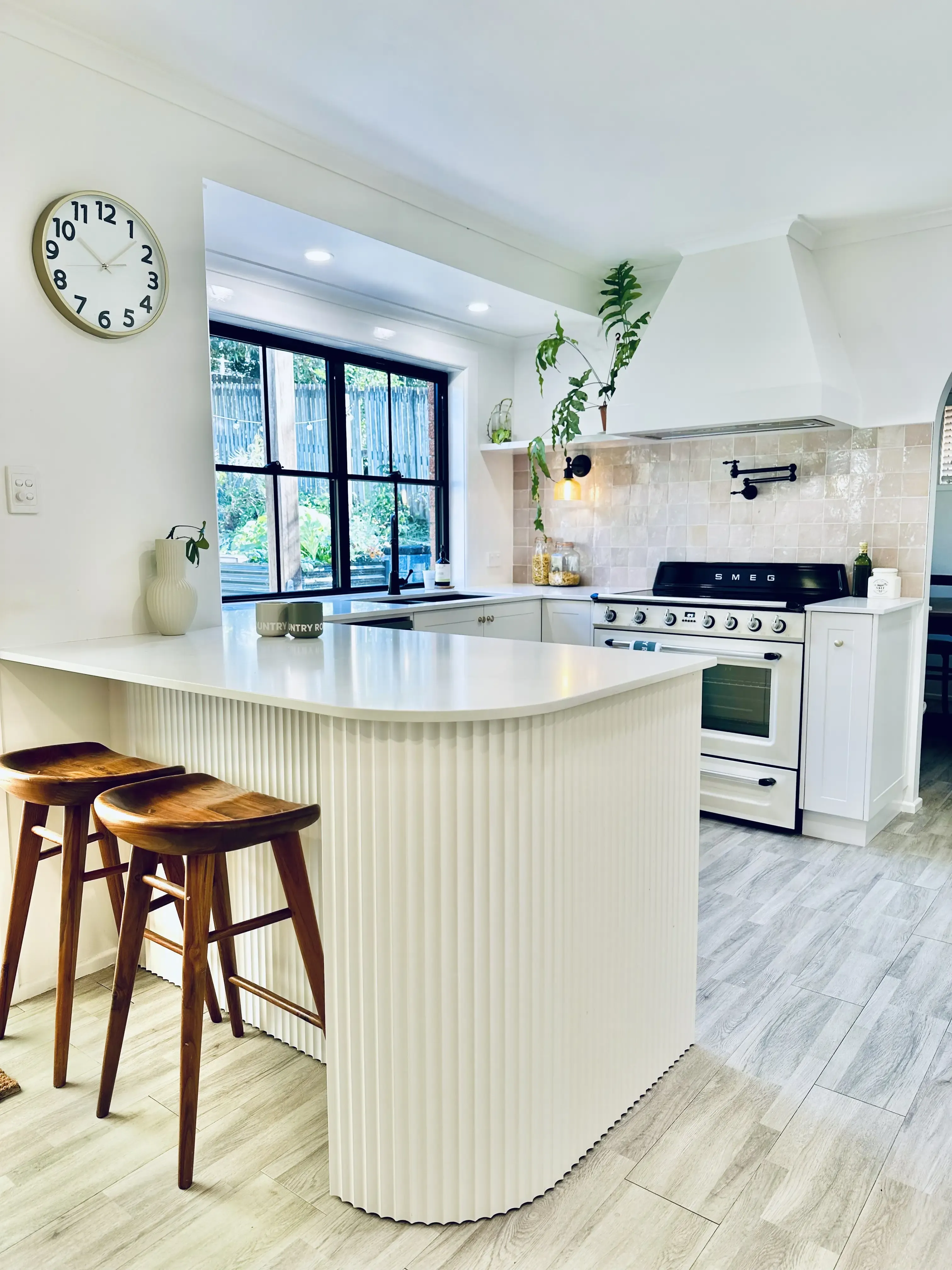 Grey Kitchen Design by Haddons Kitchen utilising lots of natural light and white theme colour to keep the space bright. the island has scalloped feature below the countertop to add texture with natural wood stools. the large range is a great feature addition