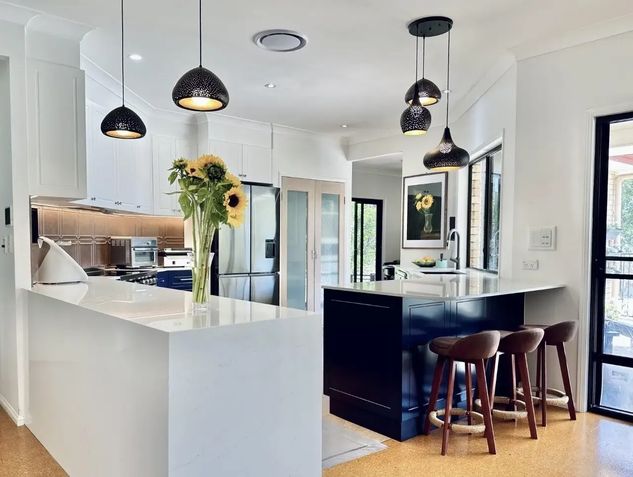 Haddon Kitchen Design showing white main colour with splash of dark blue for the breakfast bar. offset with black intracate design pendant lightshades over the main island and featuring a beautiful grey pattern design tiles for splashback. 