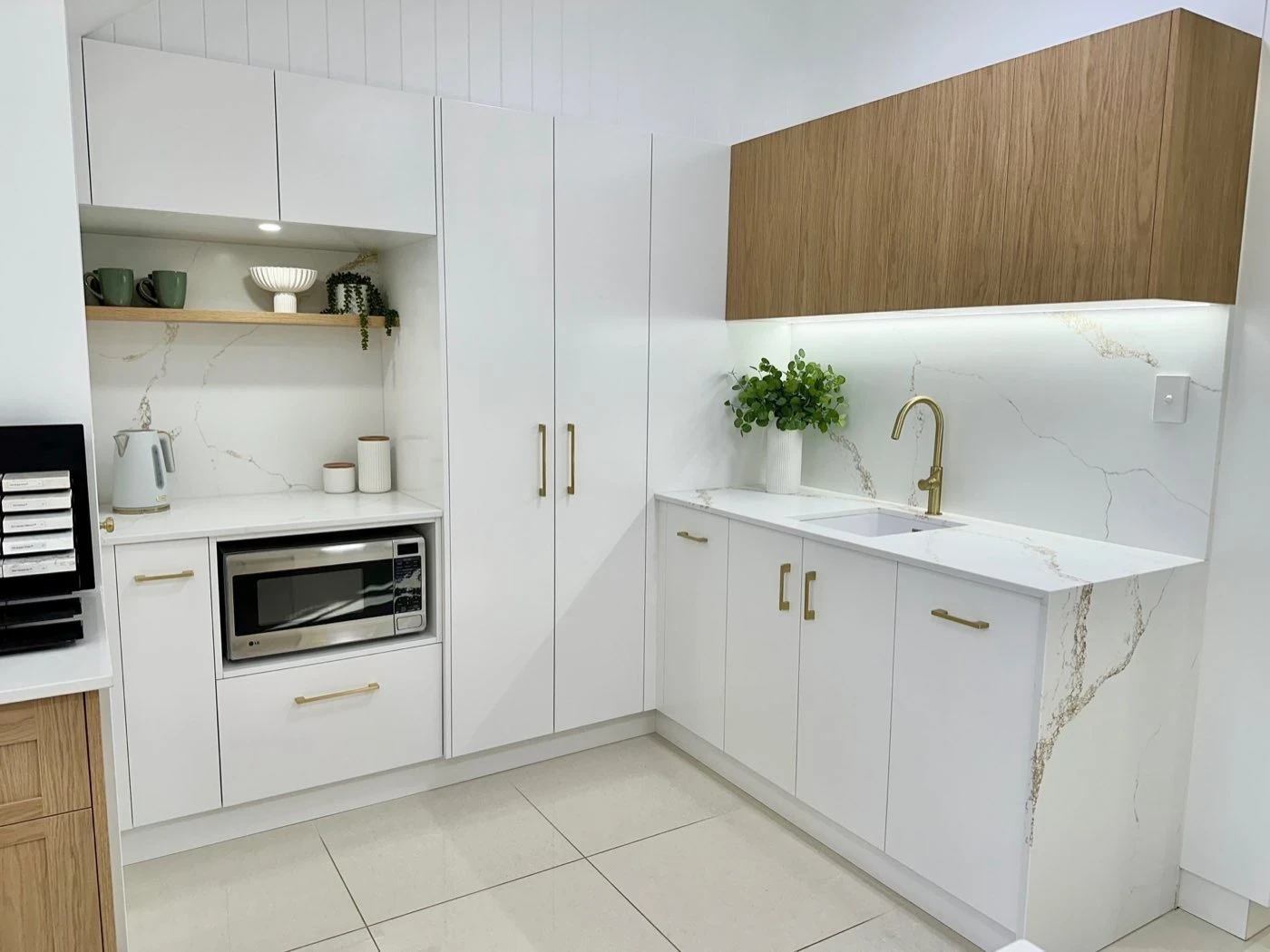 Handleless white cabinetry with brushed brass hardware and marble look splashback
