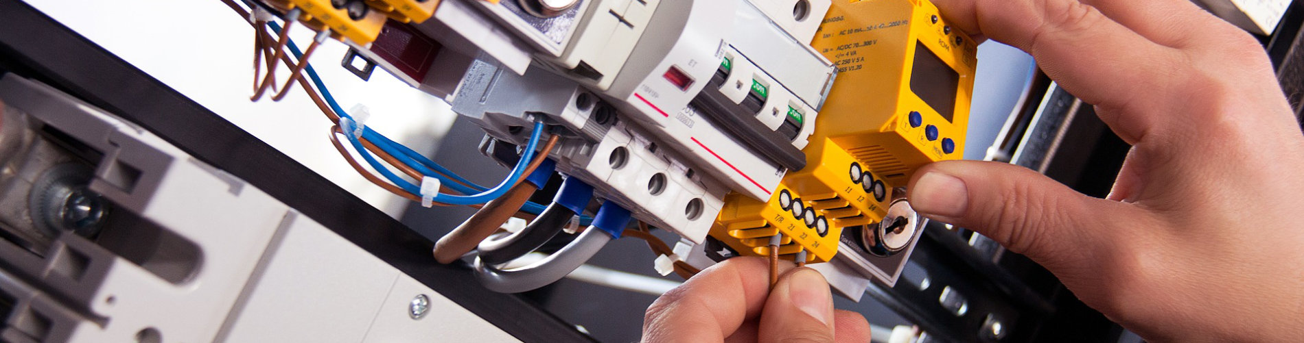 All Purpose Trade Solutions Electrician in branded uniform holding a screwdriver and inspecting electrical components of a switchboard