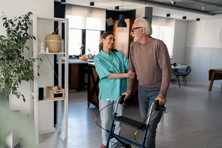 The Impact of Proper Home Modifications on Quality of Life - Home modifications reduce hours of care provided by 42% per week. older man using a walking frame and smiling with family member as he has improved personal independence around his home due to home modifications including bathroom mods, a ramp to his front and back door and a more accessible bedroom