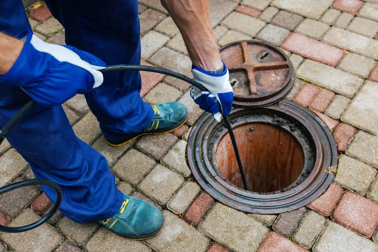 Drain rod being lowered into a blocked drain pipe by a drainage specialist to unblock the pipe