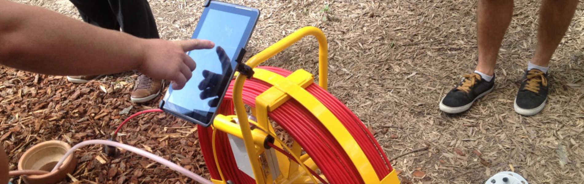 Specialist Drain plumber using cctv drain camera to conduct a drain inspection. The drain camera is down the pipe locating the blockage and a tablet shows the images to a specialist drain plumber