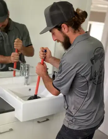 plumber using a plunger in a bathroom sink