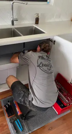 plumber fixing leak under kitchen sink