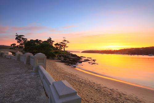 A serene view of Balmoral Beach, with its gentle waves lapping against the shore and the historic Balmoral Rotunda standing elegantly in the background. Families and friends enjoy the sunshine and the soft sand, making the most of the idyllic beach setting.