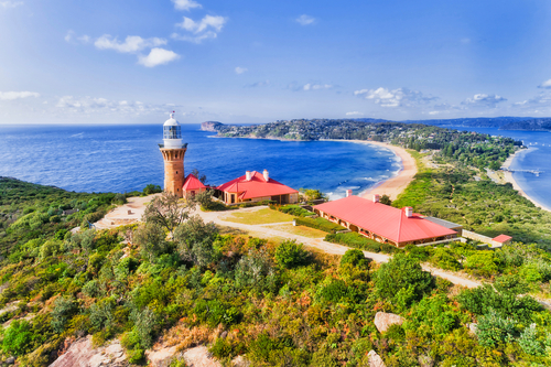 The iconic Barrenjoey Lighthouse, bathed in the golden light of sunset, stands majestically atop a rugged headland. Below, the vast expanse of the Pacific Ocean stretches to the horizon, while the natural bushland of the surrounding national park adds to the serene beauty of this historic site.