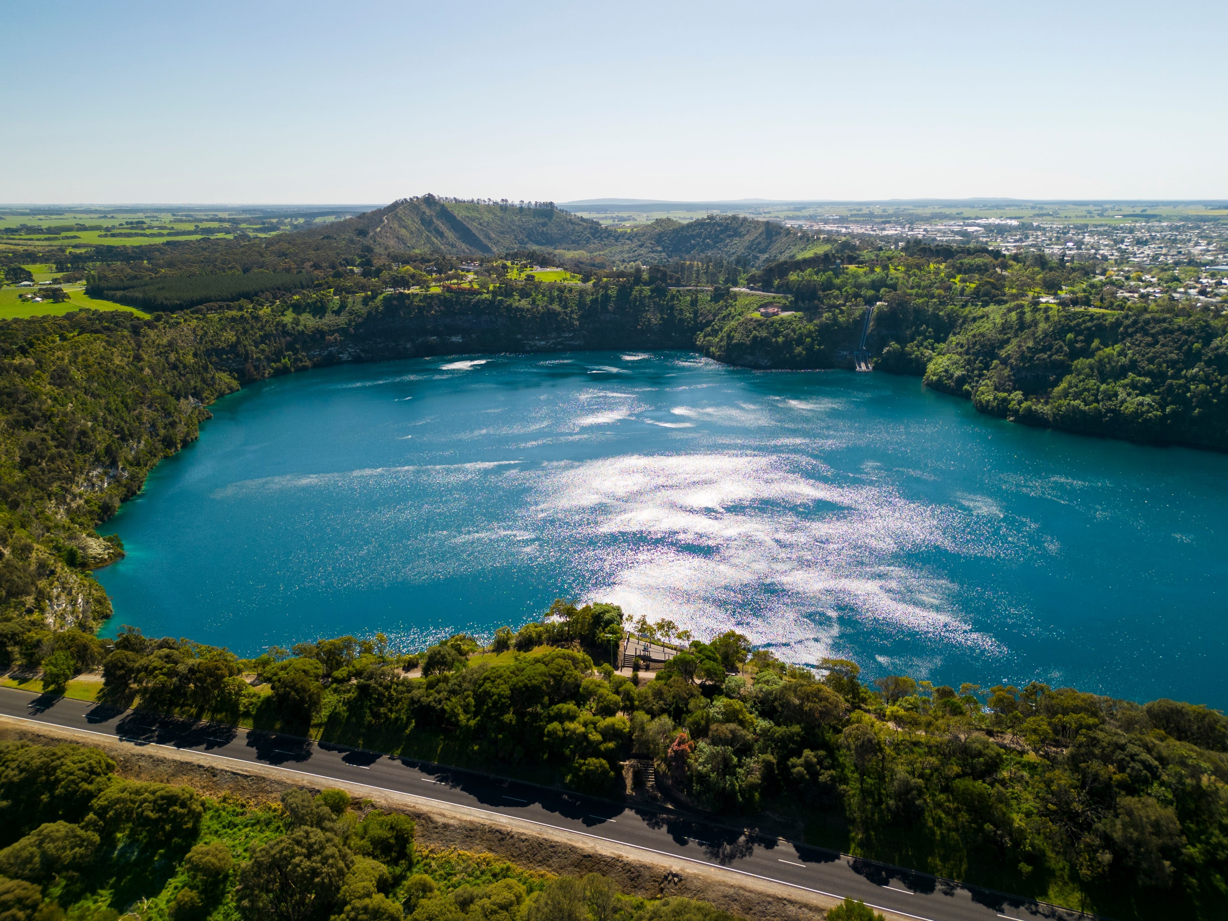 The Blue Lake shimmering under the sunlight, surrounded by lush greenery and rugged cliffs. 