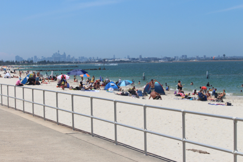 The lively scene at Brighton-Le-Sands Beach, where the golden sand meets the gentle waves of Botany Bay. Visitors enjoy the sun, swim in the calm waters, and stroll along the beachfront, with the iconic Sydney skyline in the distance, offering a perfect blend of natural beauty and urban backdrop.