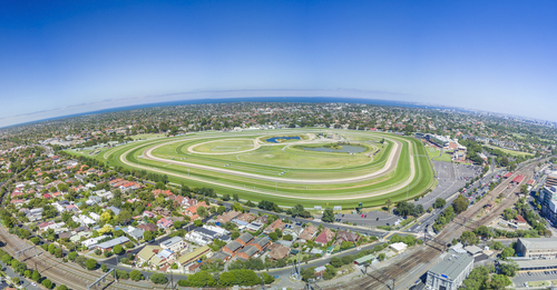 Dynamic view of a race day at Caulfield Racecourse in Southern Melbourne, featuring the excitement and vibrant crowd during a major racing event. The racecourse, a historical sports venue, is captured in full swing, with spectators and thoroughbred racers under the backdrop of the well-maintained tracks and stands. This image portrays the racecourse as a center of sporting culture and community gatherings, highlighting its importance in Southern Melbourne’s social and sporting scenes.