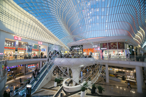 Interior view of Chadstone Shopping Centre in Southern Melbourne, displaying its luxurious design and bustling atmosphere. The image captures the spacious walkways lined with high-end boutiques and designer stores, illuminated by the natural light from the glass roof. Shoppers enjoy the diverse retail options and modern amenities, making it a premier shopping destination. This photo highlights Chadstone's elegant interior and status as 'The Fashion Capital,' reflecting its significance in Melbourne's retail landscape.