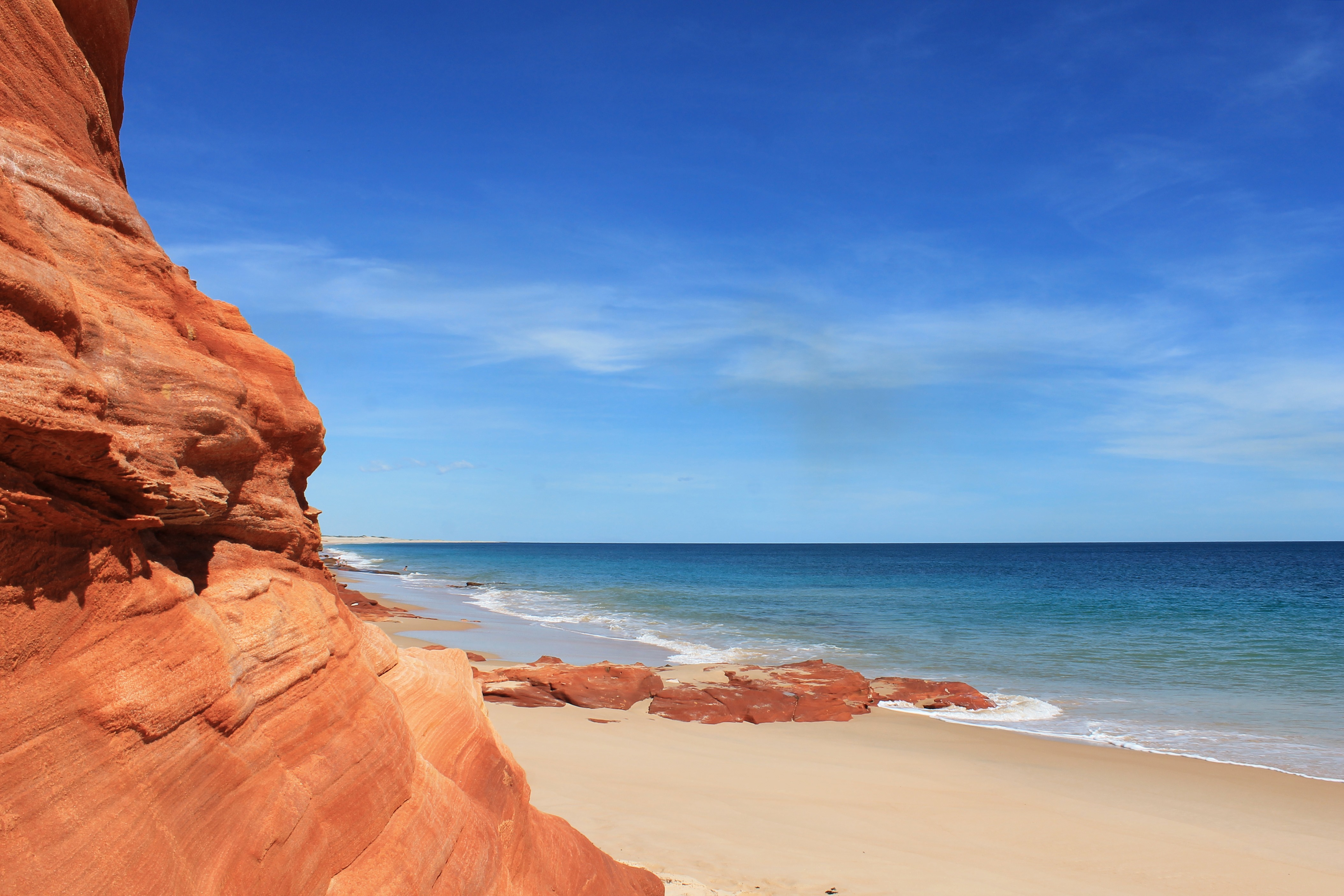 A scenic image of Coral Bay, featuring white sandy beaches and turquoise waters against a backdrop of red cliffs. 