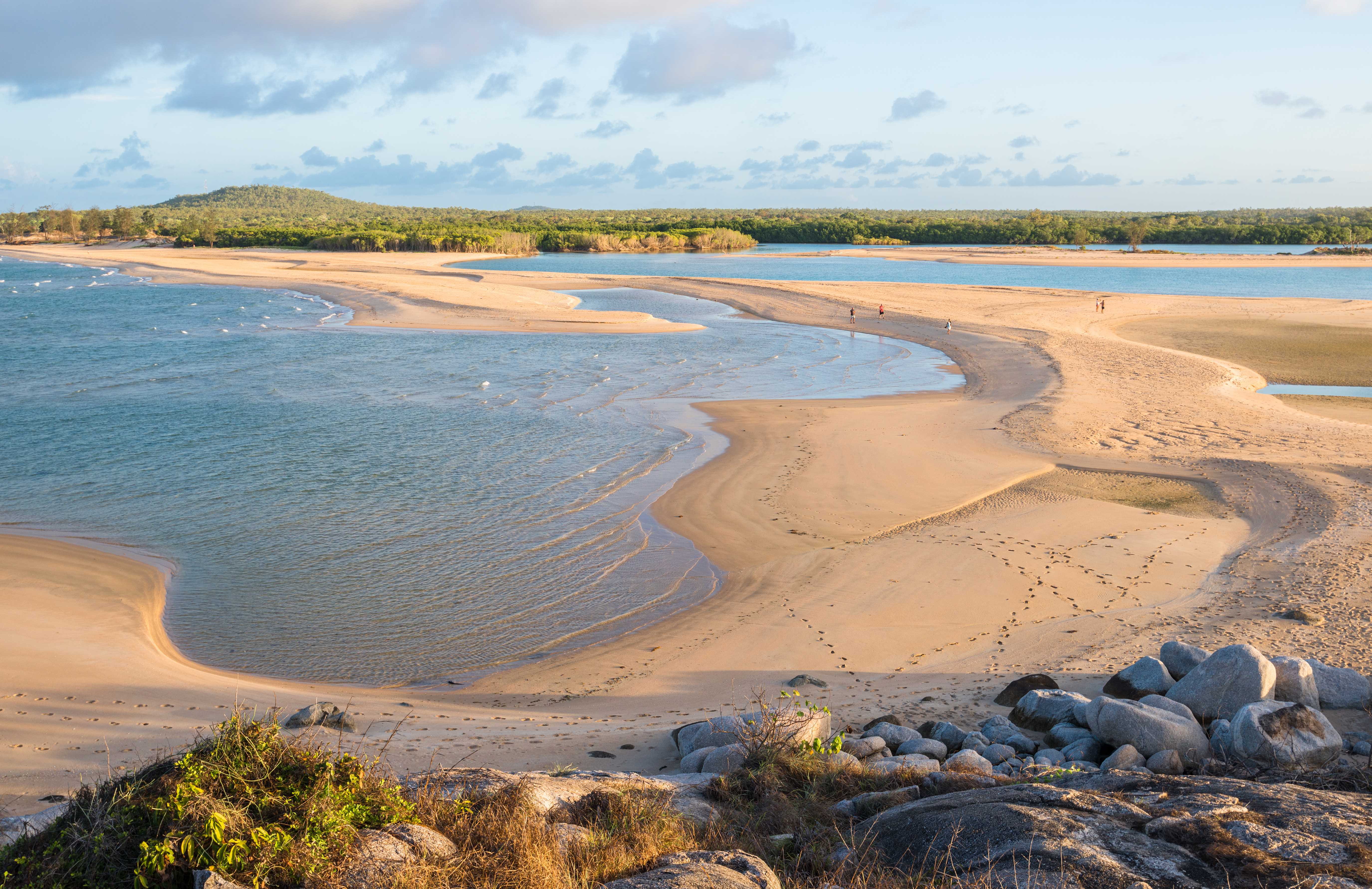 A panoramic view of a pristine beach in East Arnhem Land, with turquoise waters, white sand, and lush greenery. 