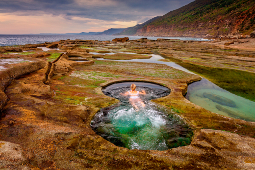 The mesmerizing sight of the Figure 8 Pools at low tide, revealing their unique shape against the backdrop of rugged cliffs and the vast Pacific Ocean. Adventurers and nature lovers traverse the rocky shoreline to witness this natural wonder, showcasing the untamed beauty of the Sutherland Shire's coastline.