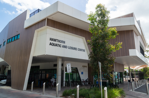 A dynamic image showing the interior of the Hawthorn Aquatic and Leisure Centre, with a focus on the modern facilities including the indoor swimming pool, where swimmers of all ages enjoy the water. The gym area features individuals engaged in various fitness activities, using state-of-the-art equipment. The design emphasizes eco-friendly elements like natural lighting and energy-efficient systems, illustrating the community’s commitment to sustainability. This image portrays the centre as a popular destination for health and fitness enthusiasts in Boroondara.
