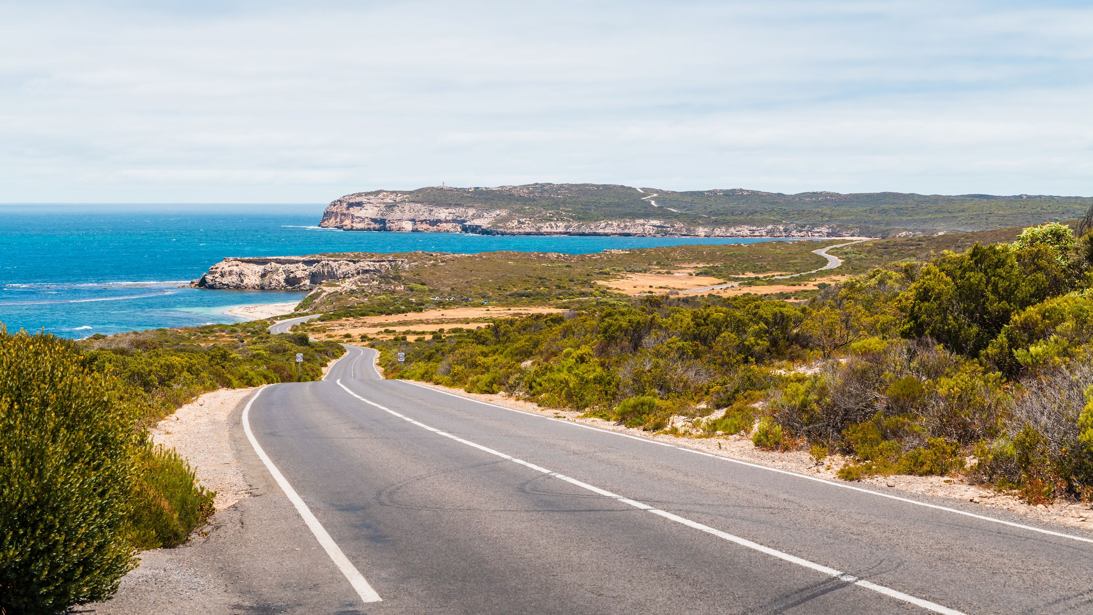  A panoramic view of rugged coastal cliffs overlooking the turquoise waters of Investigator Strait, with waves crashing against the shoreline. 