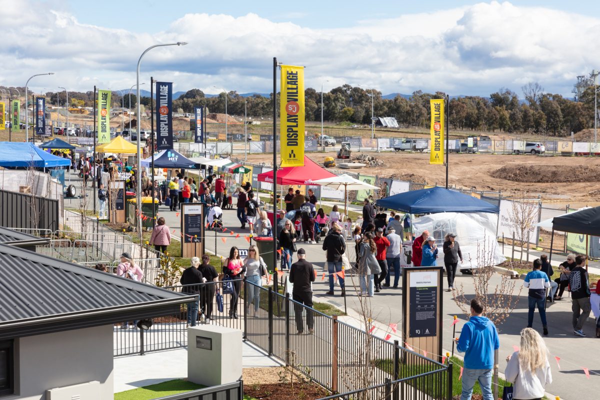 A bustling scene of Jerrabomberra Village, featuring bustling cafes, boutique shops, and outdoor dining areas bustling with activity and surrounded by leafy trees and colorful storefronts.