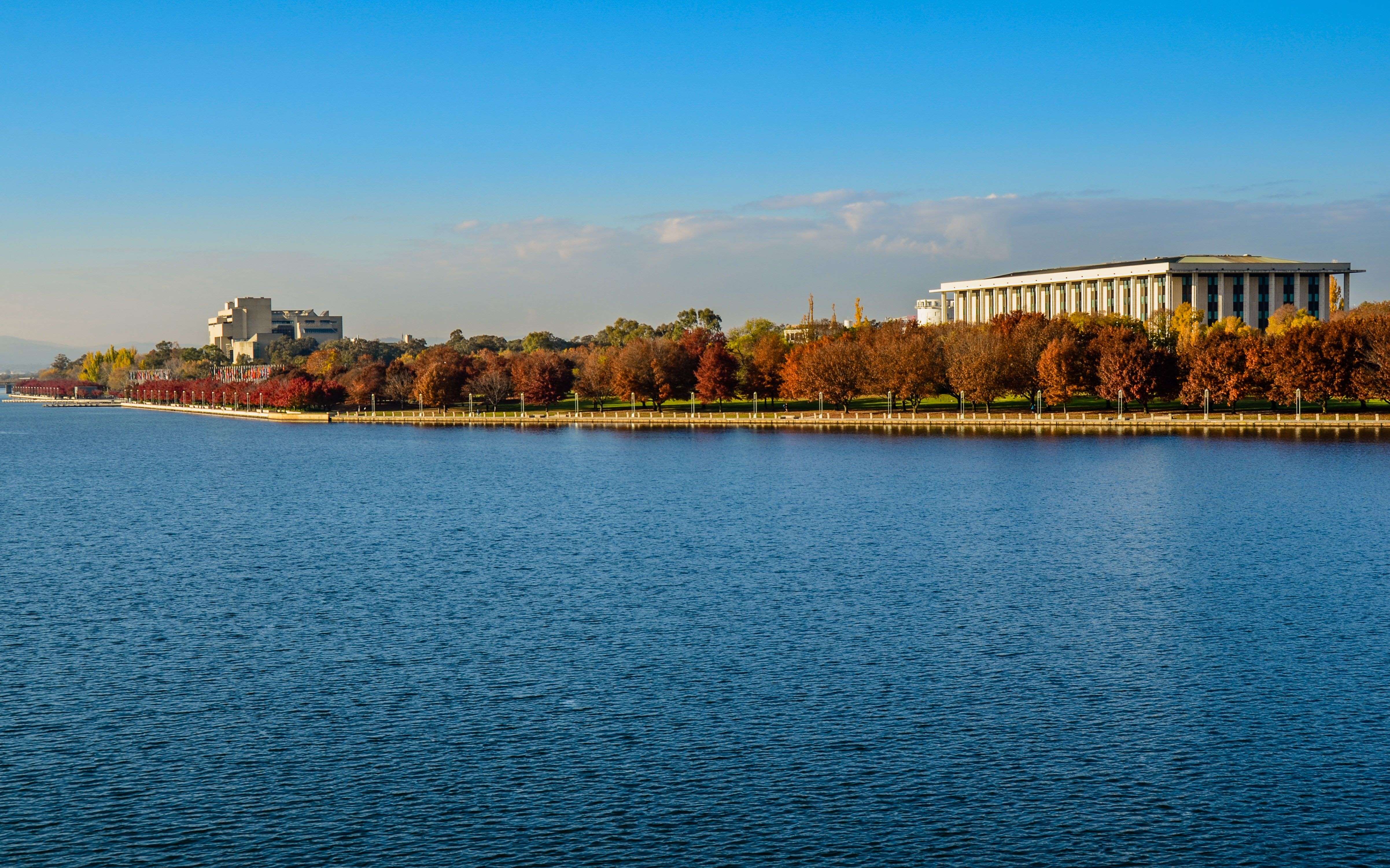  A scenic view of Lake Burley Griffin with the city skyline in the background, reflecting on the calm waters of the lake under a clear blue sky. 