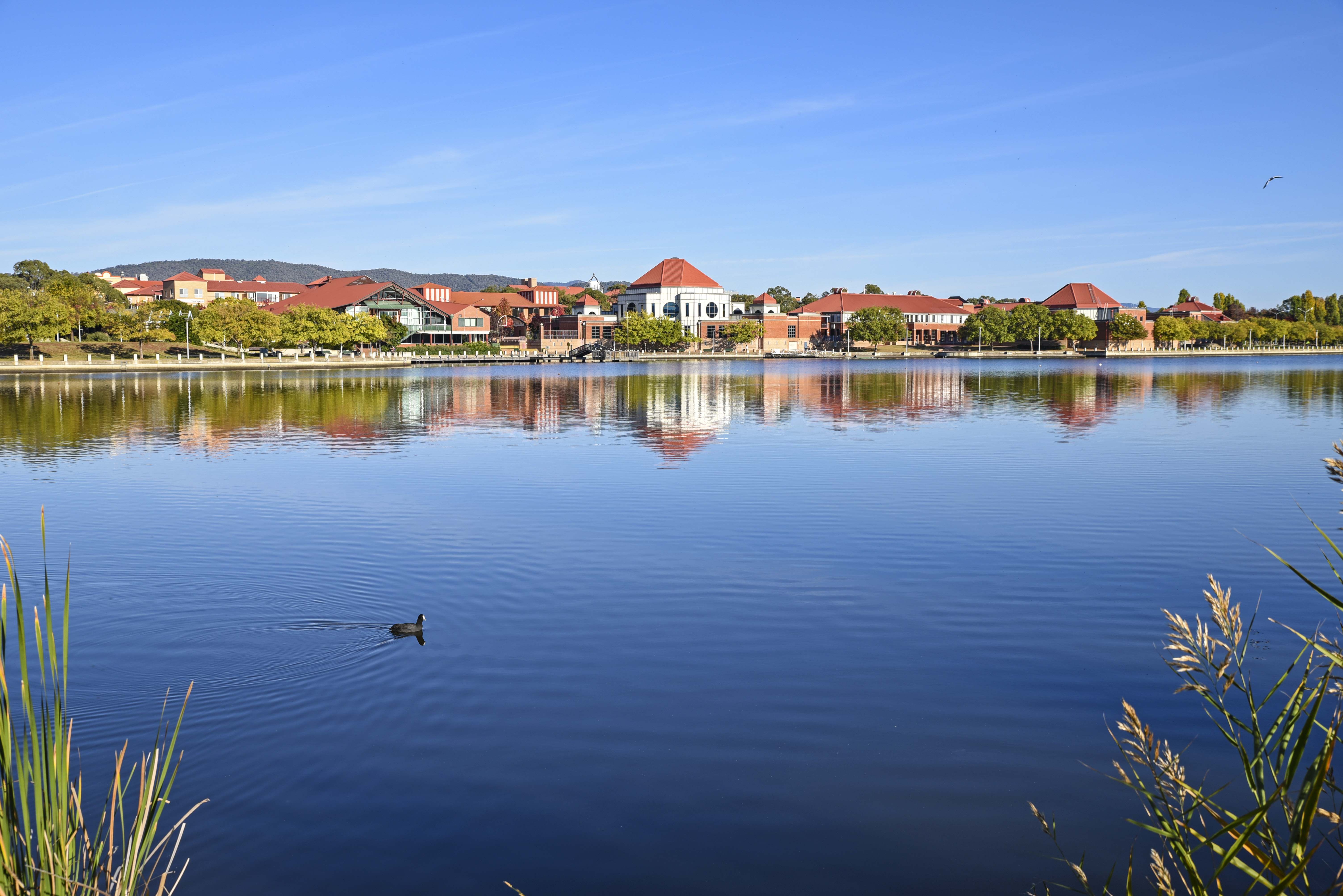 A picturesque view of Lake Tuggeranong, with the shimmering waters reflecting the surrounding greenery and distant hills, creating a serene and idyllic scene. 