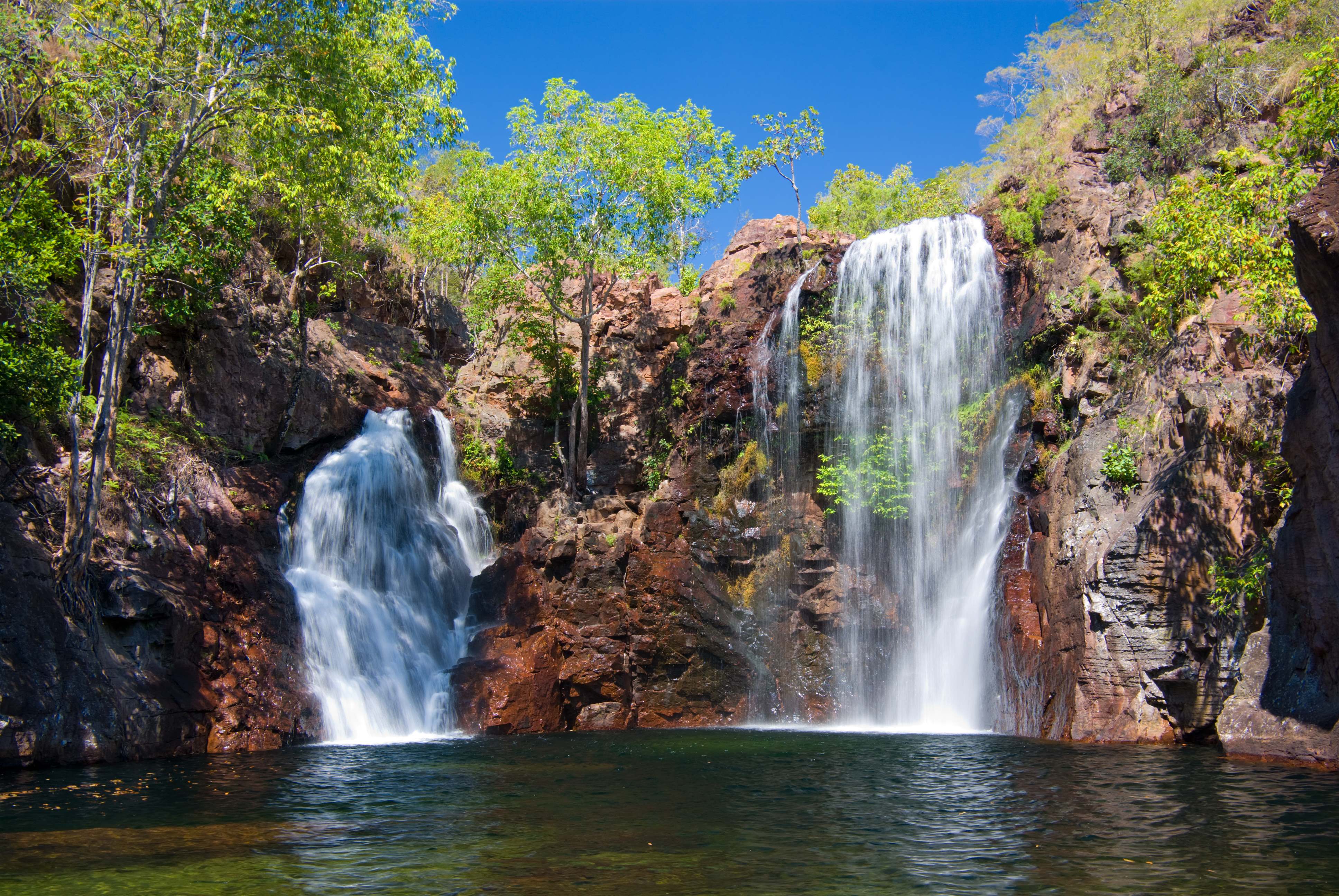 An enchanting image of Litchfield National Park's cascading waterfalls and crystal-clear swimming holes, surrounded by lush tropical vegetation and towering termite mounds, inviting visitors to explore and unwind in nature's embrace. 