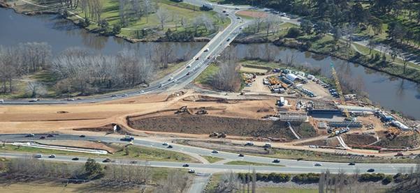 An aerial view of Majura Parkway winding its way through the scenic countryside, surrounded by lush greenery and distant mountain ranges, illustrating the seamless integration of transportation infrastructure with natural landscapes. 