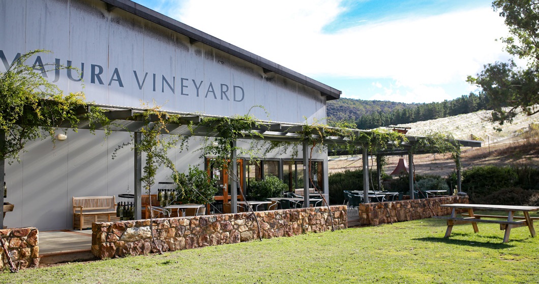 A picturesque snapshot of the Majura Winery District, featuring rows of grapevines basking in the sunlight, rustic winery buildings, and visitors enjoying wine tasting experiences amidst the scenic vineyards.