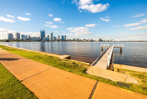 This image captures the bustling atmosphere of the Mends Street Jetty area, a focal point for locals and tourists alike seeking to explore South Perth's waterfront. The jetty extends into the Swan River, with a ferry docked and ready for passengers, symbolisng the connection between South Perth and the city center. The surrounding precinct is lively with outdoor dining, shops, and people enjoying the waterfront ambiance, set against the backdrop of Perth's skyline.