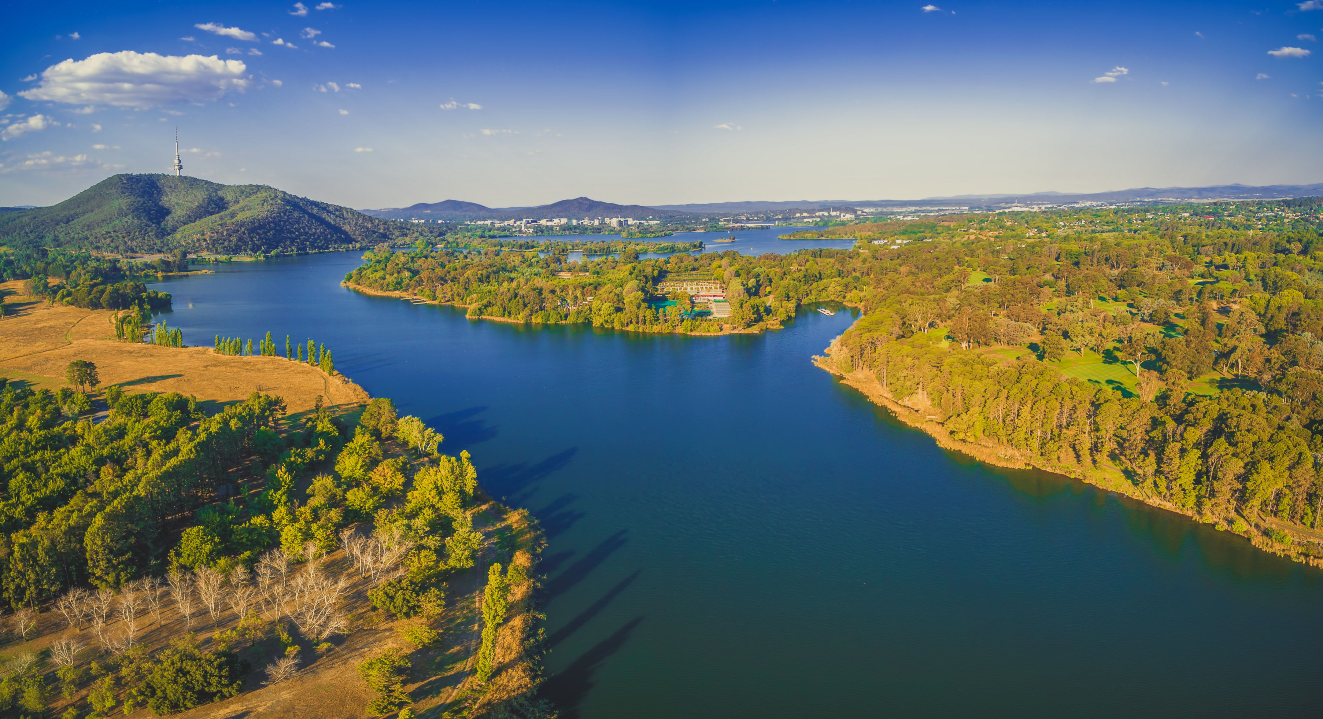 A serene image of the Molonglo River meandering through the valley, flanked by lush greenery and framed by the distant hills, illustrating the natural beauty and tranquility of the region. 