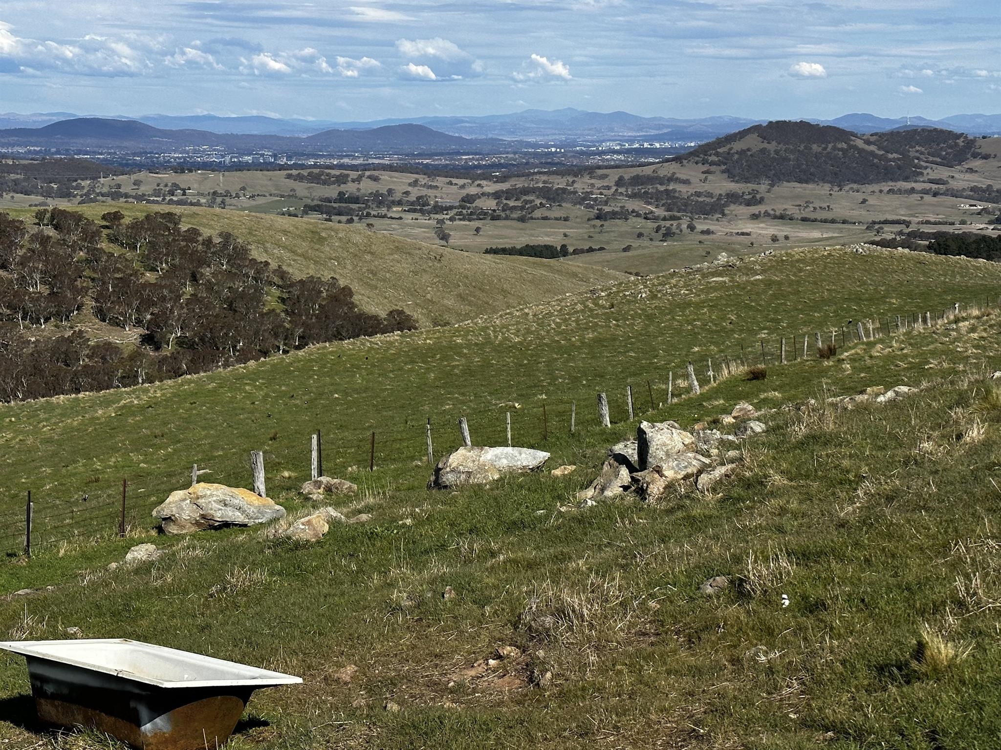 A breathtaking image of Mount Majura showcasing its rugged terrain, verdant slopes, and panoramic views of the surrounding landscape, with the iconic Brindabella Ranges visible in the distance. 