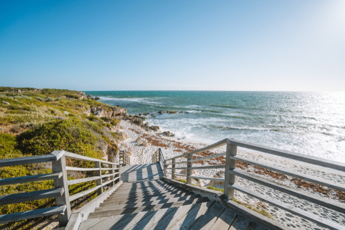 Depict the pristine conditions of Mullaloo Beach with its clear blue waters, white sandy shores, and people engaging in various activities such as surfing, swimming, or simply relaxing under the sun, showcasing the beach's popularity and family-friendly foreshore.
