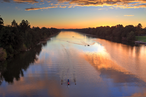 The tranquil Nepean River at dusk, with its gentle waters reflecting the soft colours of the sunset. The riverbanks are lush and inviting, with people enjoying leisurely walks and the serene environment, highlighting the river's role as a cherished natural haven in Penrith.