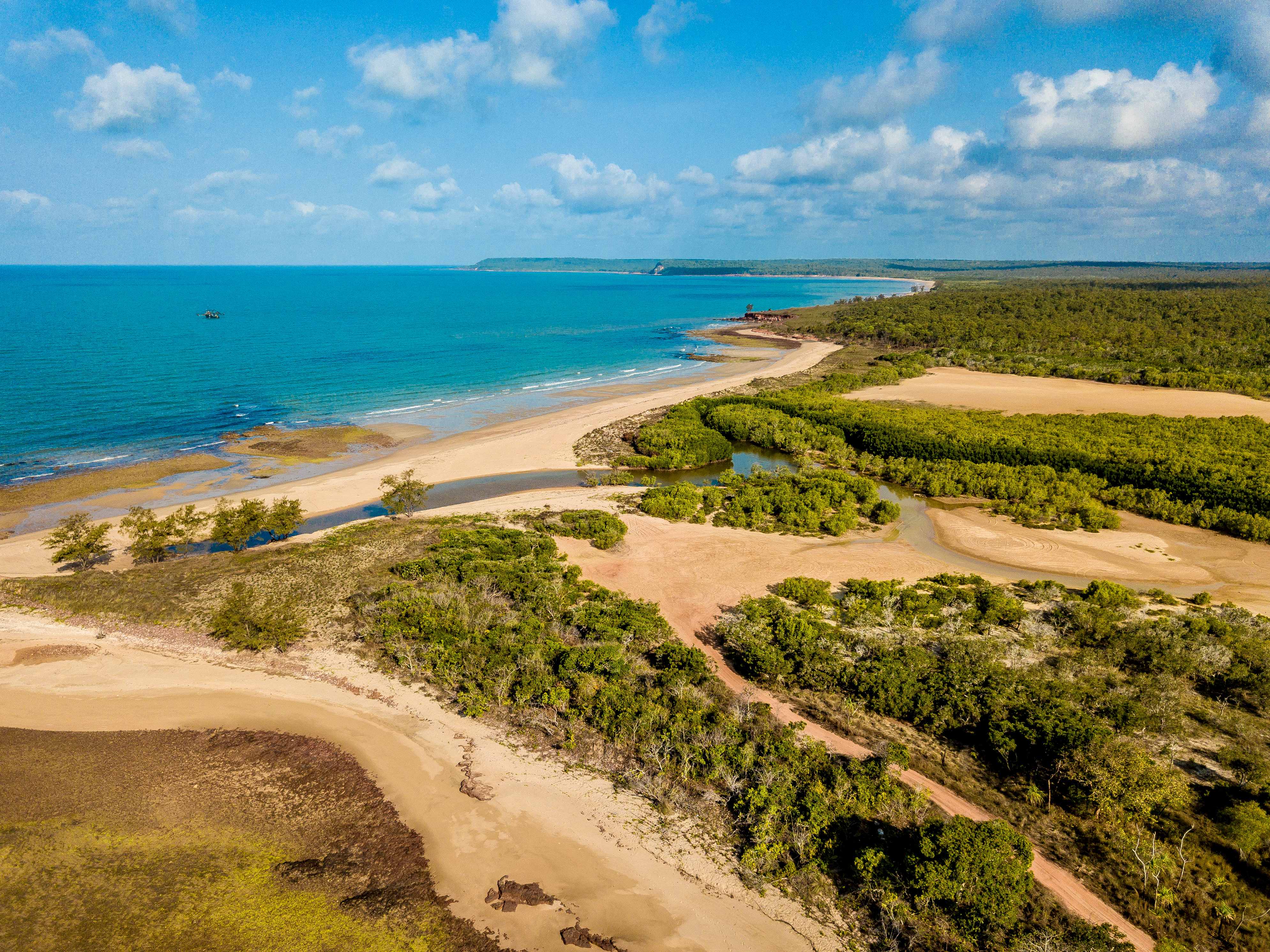 A photo of the coastline of Nhulunbuy, with turquoise waters, white sandy beaches, and lush greenery. 
