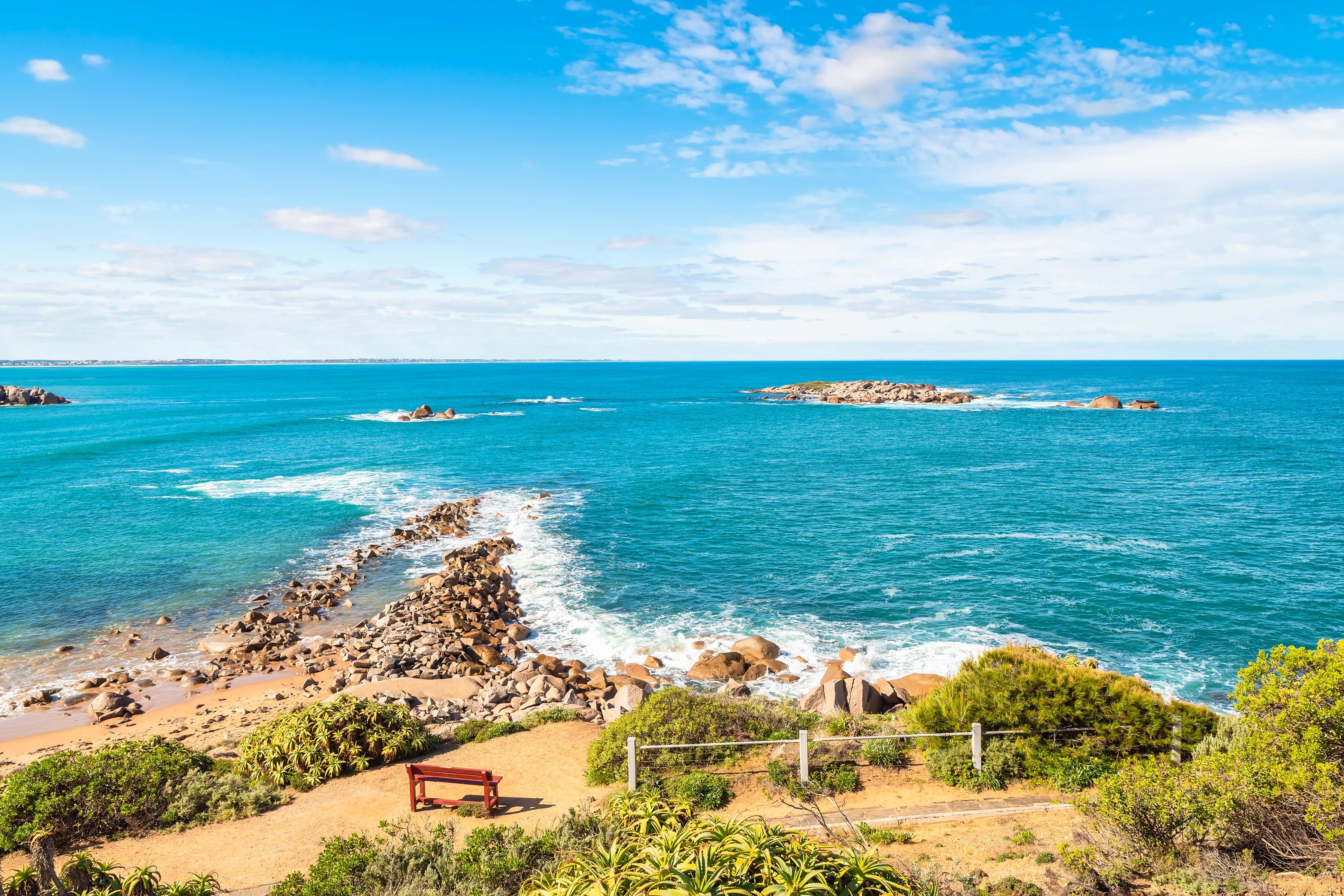A panoramic view of a pristine beach with turquoise waters, bordered by rocky cliffs and lush vegetation. 