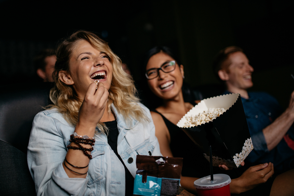 An image capturing two females enjoying a movie at Reading Cinemas within Woodgrove Shopping Centre. They are seated comfortably, immersed in the film, with one of them holding a large popcorn bucket. The ambient lighting of the cinema casts a soft glow, enhancing the cozy and intimate atmosphere. The modern decor of the cinema, with plush seating and advanced audio-visual equipment, underscores the premium movie-going experience offered here. This scene effectively illustrates the entertainment and joy that Reading Cinemas provides to its patrons, making it a popular destination for movie lovers in Melton.