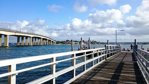 The tranquil beauty of Sans Souci Pier at dusk, with the setting sun casting a golden glow over the calm waters. People gather to fish, enjoy the peaceful atmosphere, and watch as the day slowly transitions to night, reflecting the serene and leisurely pace of life in the St George area.