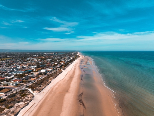An image capturing the sun-drenched expanse of Semaphore Beach with its inviting golden sands and crystal-clear waters. Families enjoy the beachfront, children play near the water's edge, and in the background, the vintage carousel spins, while the classic jetty extends into the sea, offering a picturesque view that harks back to the area's historic charm as a seaside resort. This scene encapsulates the family-friendly and leisurely atmosphere of Semaphore Beach, making it a beloved destination in the Western Suburbs of Adelaide.