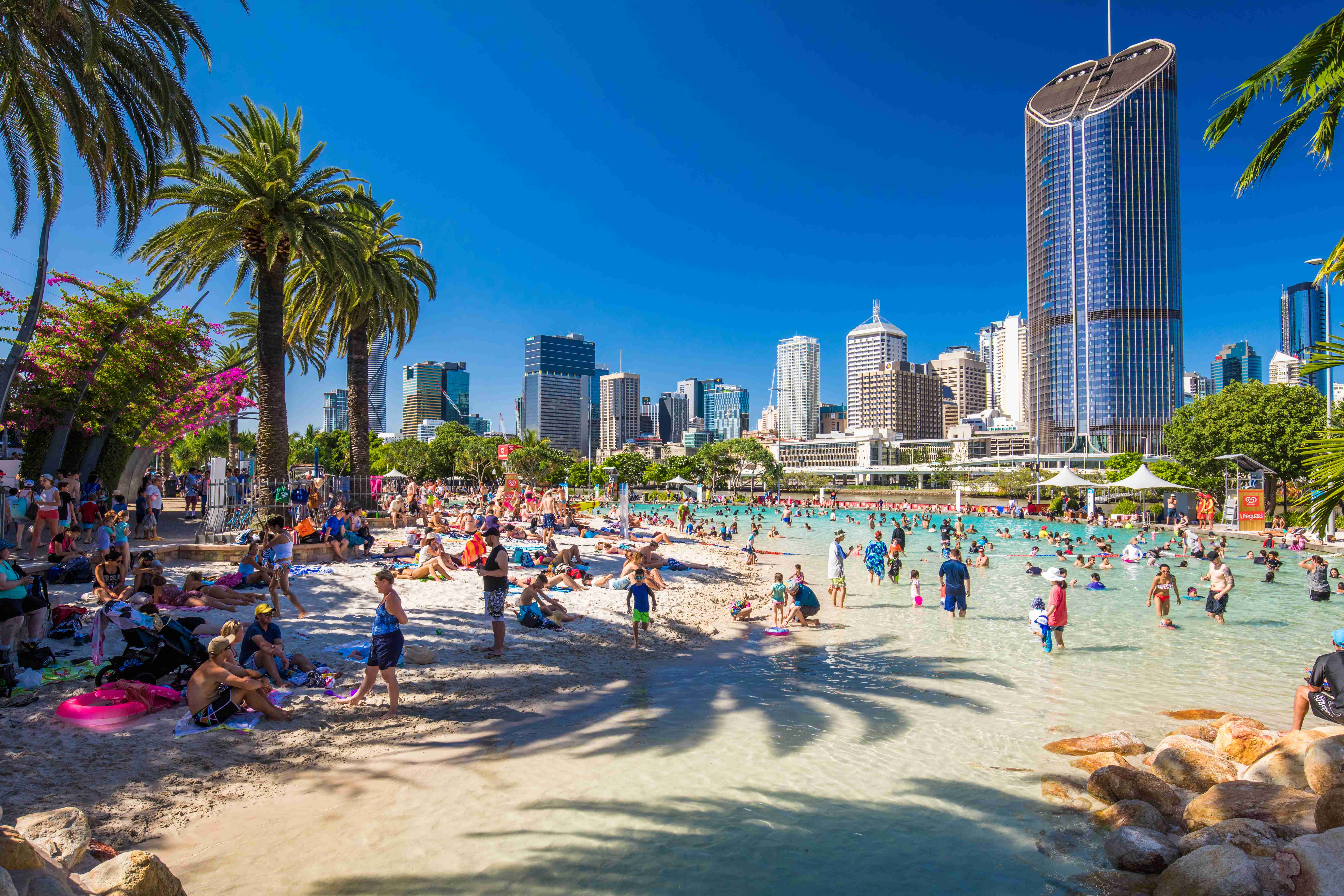  A serene image of South Bank Parklands during the day, featuring people enjoying the riverside promenade, lush greenery, and various recreational facilities. 