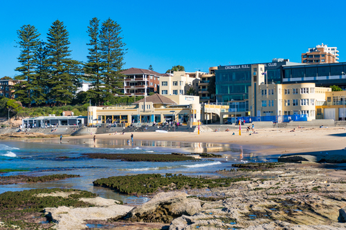 A vibrant day at South Cronulla Beach, where sunbathers, surfers, and swimmers enjoy the sun-kissed sands and rolling waves. The beachfront esplanade buzzes with activity, from joggers and skaters to families enjoying the outdoor cafes, embodying the spirited and welcoming community of Cronulla.