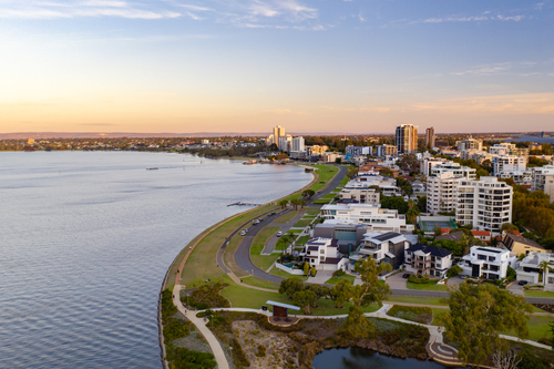 The South Perth Foreshore comes to life in this image, offering a panoramic view of the serene Swan River with the stunning Perth city skyline in the distance. People are seen enjoying various activities, from picnicking on the green lawns to cycling along the scenic paths. The area's natural beauty is accentuated by public art pieces and flowering gardens, making it a picturesque setting for relaxation and leisure.