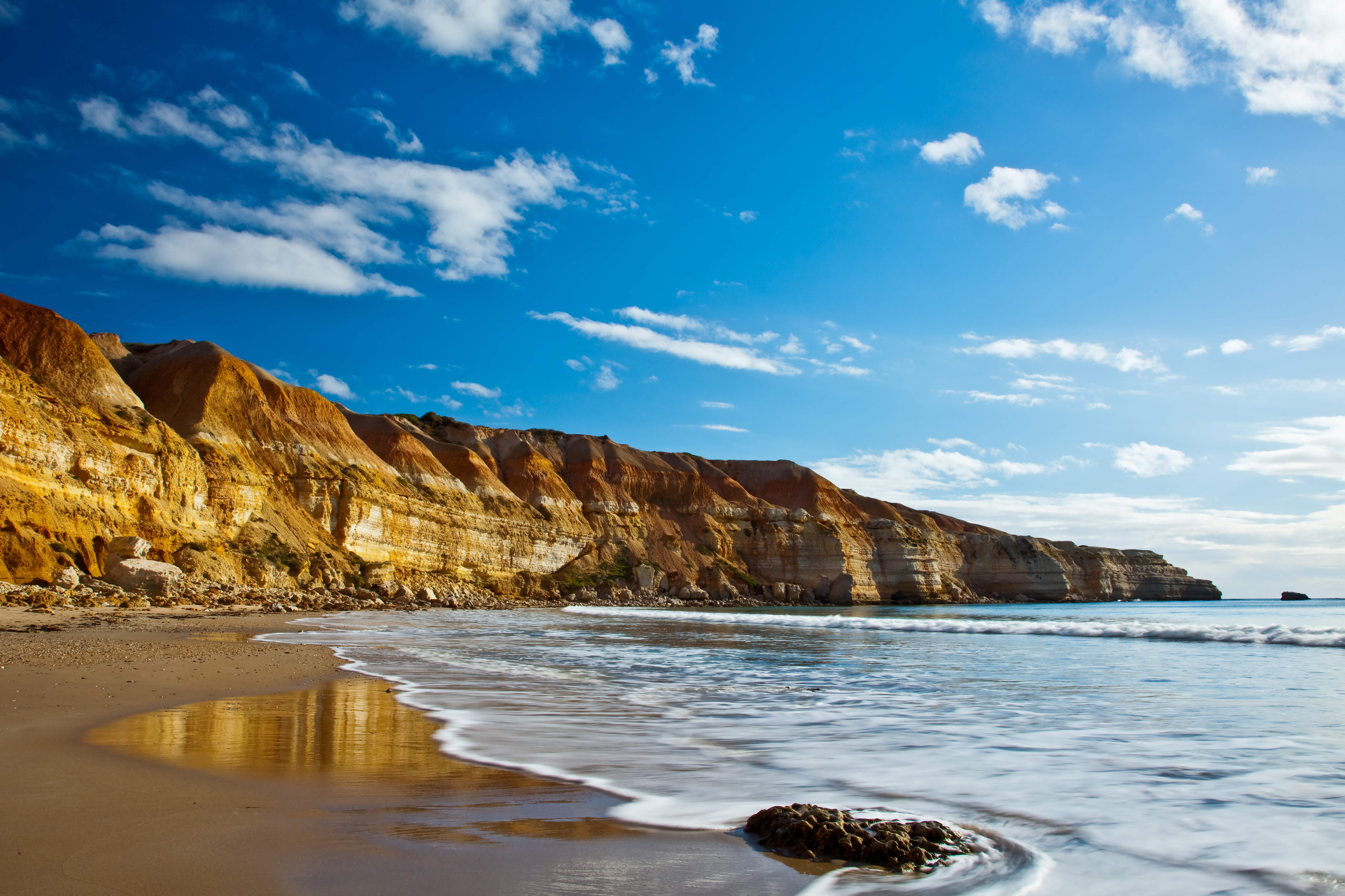 A panoramic view of a secluded beach with golden sands, framed by towering cliffs and the azure waters of the Southern Ocean. 