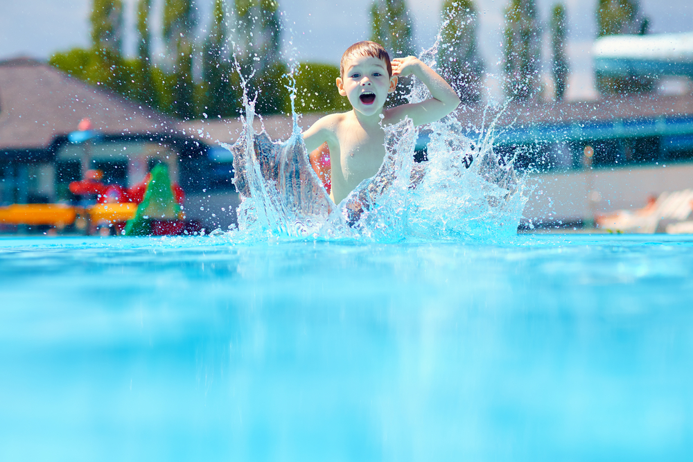 A vibrant image depicting a child joyfully playing in the outdoor pool at Splash Aqua Park and Leisure Centre. The child, mid-laughter, splashes water while enjoying the interactive water features, such as water jets and mini slides, under the bright sun. The pool's colorful surroundings and the presence of other families enhance the atmosphere of fun and engagement, making it a popular summer destination. This photo captures the essence of family-friendly recreation, showcasing the leisure centre as a perfect place for children and families to cool off and have fun.