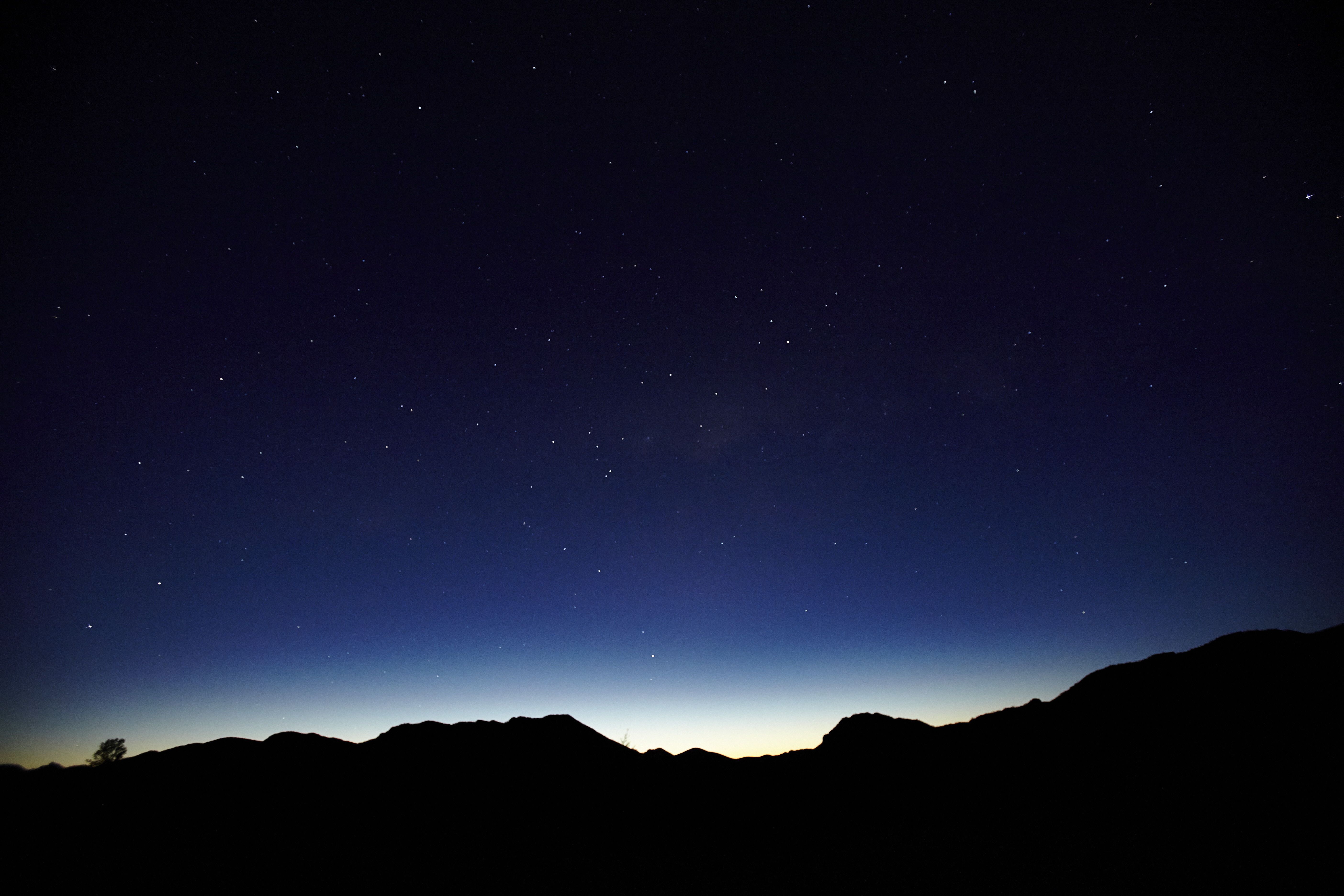 A long exposure photograph capturing the Milky Way arching over the silhouette of a rugged mountain range. 