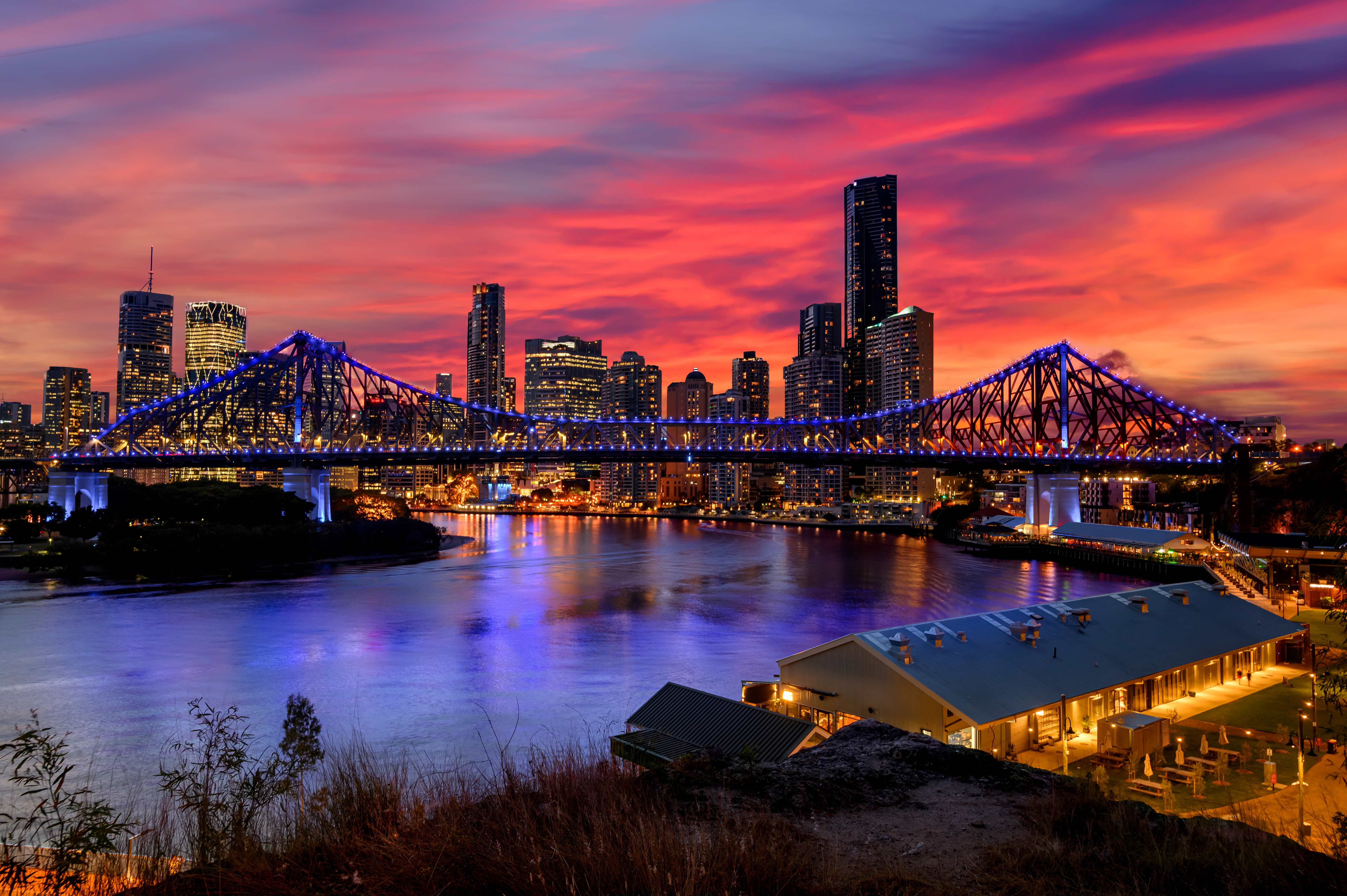 The Story Bridge illuminated against the night sky, showcasing its distinctive architectural features and its reflection in the Brisbane River. 