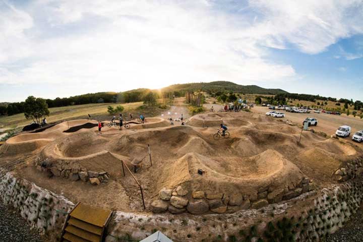 An aerial view of Stromlo Forest Park showcasing its vast expanse of woodlands, winding trails, and mountain biking tracks, with visitors enjoying outdoor activities amidst the scenic landscape.