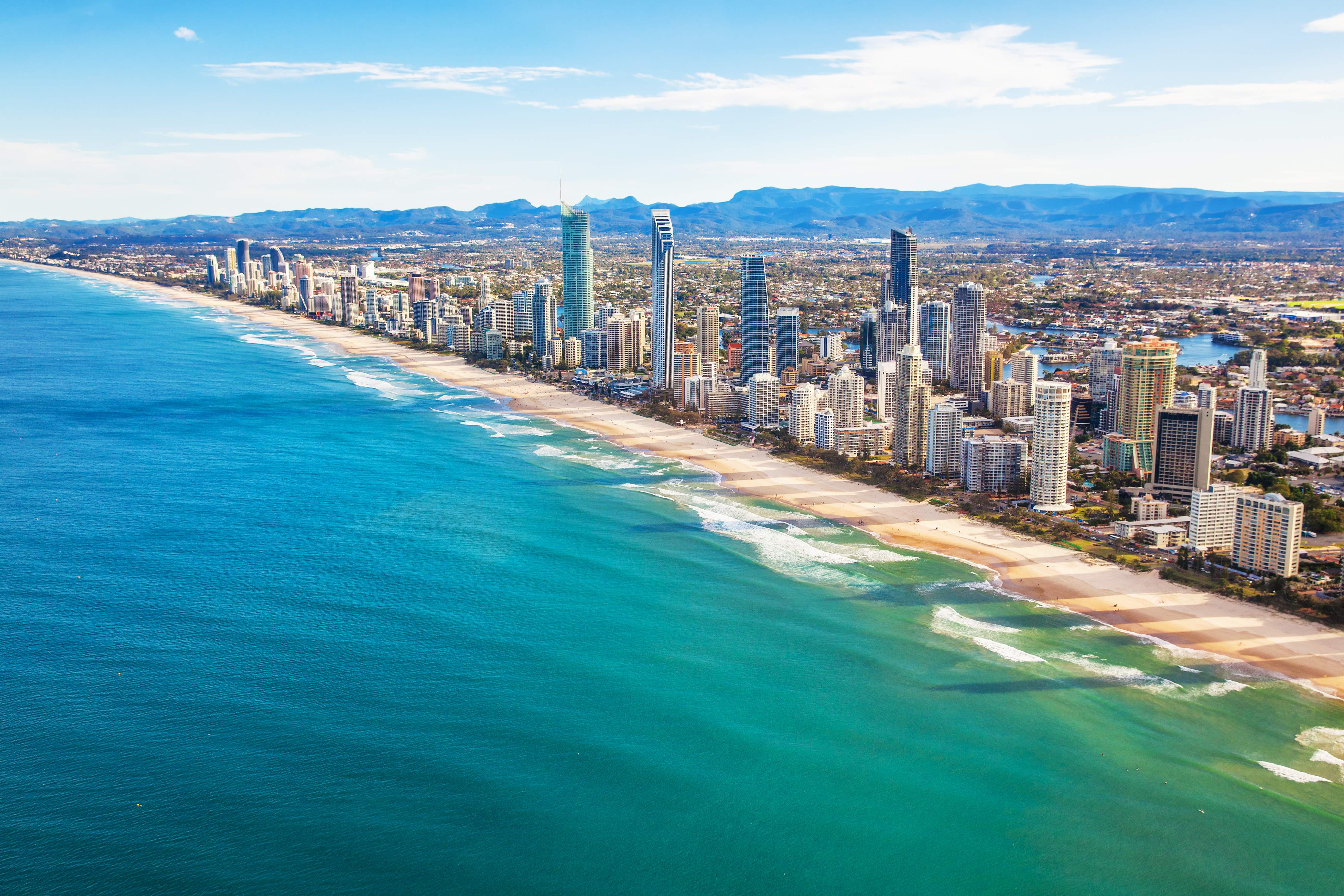 A picturesque scene of Surfers Paradise Beach, featuring golden sands, rolling waves, and a backdrop of high-rise buildings. 