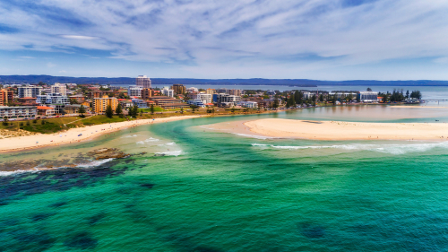 A picturesque view of Terrigal Beach, showcasing its golden sands and sparkling blue waters, framed by the vibrant Central Coast shoreline, epitomizing the region's stunning beachside allure. 