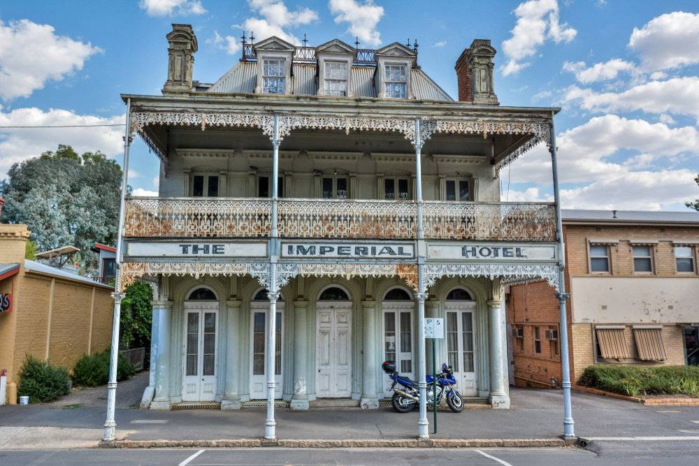 A vibrant image of The Imperial Hotel in Castlemaine, illustrating its charming historical facade that dates back to the gold rush era. The hotel's prominent position on a busy street corner, adorned with ornate detailing and period features, captures the essence of a bygone era. This establishment is depicted bustling with activity, suggesting its role as a popular social gathering spot in the town, offering a glimpse into the lively local culture and hospitality.